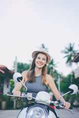 Fototapeta na wymiar Riding lifestyle. Outdoor portrait of pretty young woman in hat sitting on scooter.