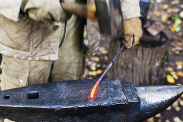 Blacksmith hammering red hot iron rod on anvil