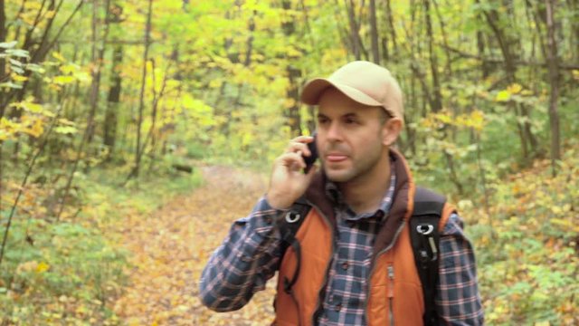 Young Man With talking on the phone Looking For Direction On The Forest. Caucasian male outdoors in nature. Hiker young man with backpack  in autumn forest.