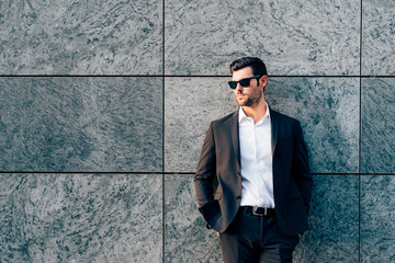 Young handsome modern businessman posing leaning against a wall, looking in camera, wearing a coat...