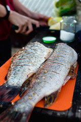 Woman cut up the fish and put spices inside big freshly caught and gutted fish on orange board in nature. One of the moments of cooking in hike Close up shot