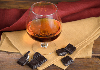 Glass of brandy and a chocolate on wooden table