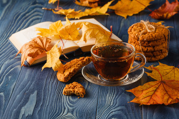 Cup of tea with old book, autumn leaves on wooden table