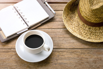 Work at Home - Black coffee in white cup with blank note book and woven hats.