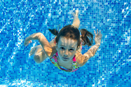 Child swims in pool underwater, happy active girl has fun under water, kid sport on family vacation
