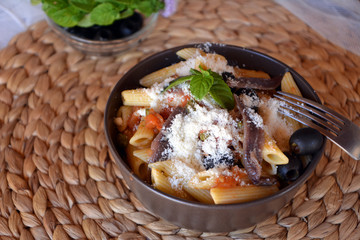 Delicious italian food penne ala puttanesca on a bowl on a table.