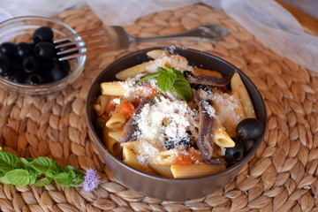 Delicious italian food penne ala puttanesca on a bowl on a table.