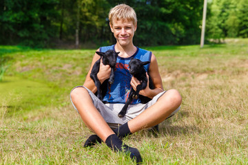 Happy teenager boy holding little black baby goats in the meadow