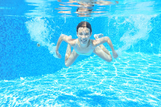 Child swims in pool underwater, happy active girl has fun under water, kid sport on family vacation
