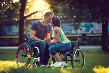 Handicapped young couple on two wheelchairs kissing .