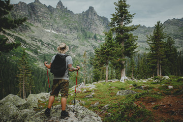 Hiker young man with backpack and trekking of cliff and looking