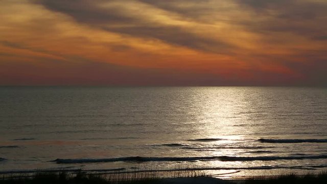 The sky over the ocean glows with early morning color reflecting on the sea with breaking waves on a sandy beach. Looping footage shot on Florida Coast near St. Augustine. 