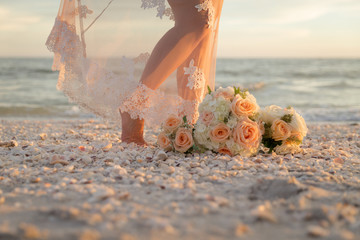 close up of bride feet, flowers and gown on beach