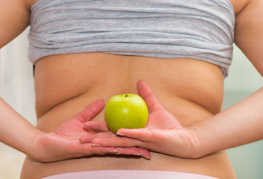 Closeup Womans Lower Back With Shirt Lifted Up, Wearing Jeans, Holding Apple Between Hands, Weightloss Concept