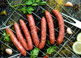 Foto auf Acrylglas Raw sausages merguez, on a black background, with spices on the gridiron © kassiya