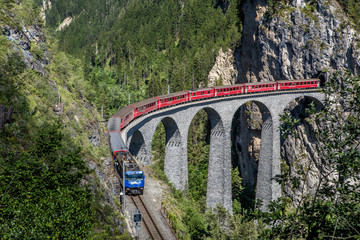 The train of Rhaetian Railway running on the famous Landwasser Viaduct into the tunnel, with view of colorful trees on a sunny autumn day, Canton of Grisons, Switzerland