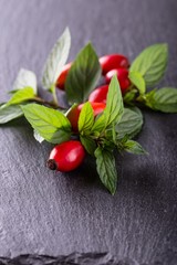 Group of red hips with green leaves on black stone