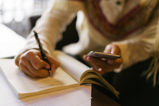 Woman writing notes and using smartphone