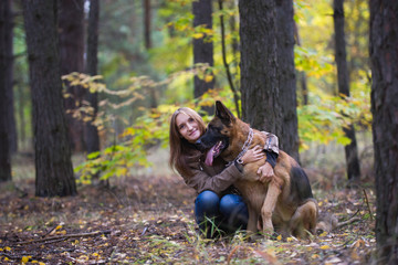 Young cute woman hugging a German Shepherd dog outdoors in the autumn forest