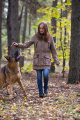 Young cute woman playing with German Shepherd dog outdoors in the autumn forest