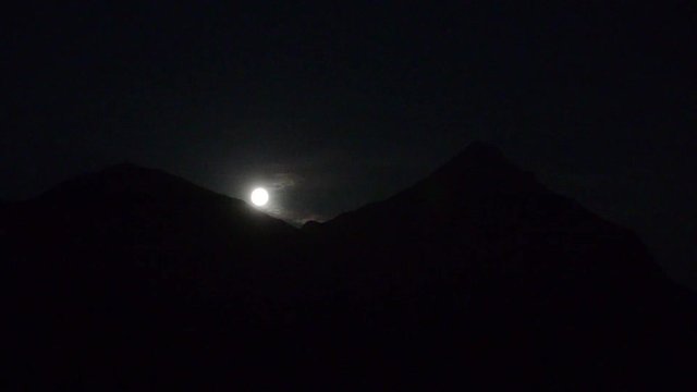 Moon rise over alps time lapse. moon comes up between two mountains.