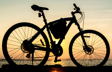 Fototapeta premium Silhouette of mountain bike at sea with sunset sky background