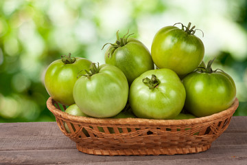 unripe green tomatoes in a wicker basket on wooden table with blurred background