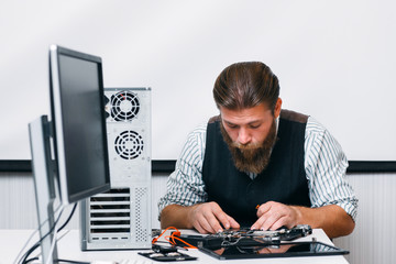 Bearded engineer assembling computer at workplace. Repairman fixing computer inside circuit in office. Electronic renovation, technology, business concept