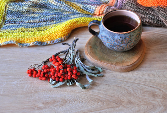 A cup of tea, rowan bunch and knitted plaid on wooden background. Чашка чая, кисть рябины и вязаный плед на деревянной поверхности.