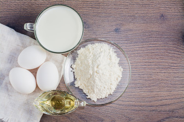 Куриные яйца, мука, молоко и масло на деревянном фоне