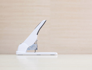 Closeup white stapler , office equipment on blurred wood desk and wall in office room textured...