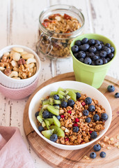 Healthy breakfast; Homemade granola with kiwi, blueberries and nuts in white bowl