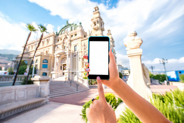 Naklejka premium Holding smart phone with white screen on Monte Carlo Opera building backgraound in Monaco