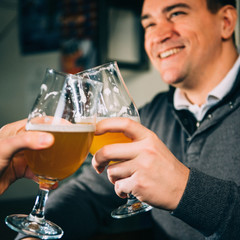 Beer toast. Young man having a beer in pub, toasting with friend. Focus on glasses