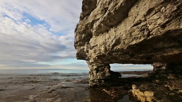 An arch rock formation on the Lake Michigan coast of Wisconsin's Door County, Michigan is backed by a dramatic cloudy blue sky and gently lapping waves. Looping. 