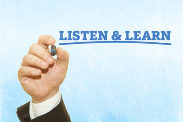 Businessman hand writing LISTEN AND LEARN message on a transparent wipe board.