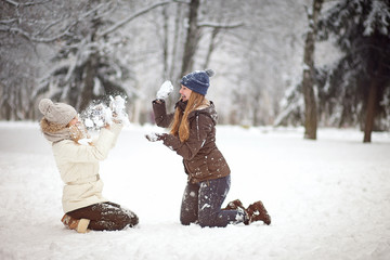 Fototapeta na wymiar Two girls friends or sisters playing snowballs in the snow in the winter in a warm winter clothes