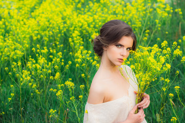 Portrait of young beautiful girl in field with bouquet of yellow flowers in hands looking to the camera