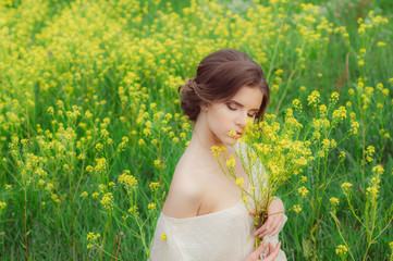 Portrait of young beautiful girl in field with bouquet of yellow flowers in hands with closed eyes