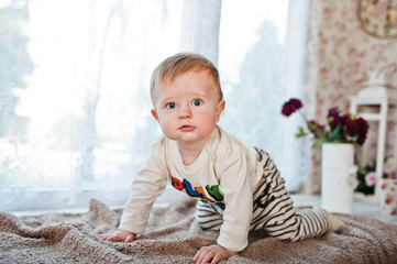 Fototapeta premium Cute little caucasian baby boy creeps on coverlet and looking at