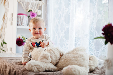 Cute caucasian baby boy sitting on windowsill with soft toy dog