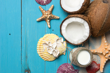 Fresh coconuts, coconut oil in a jar, shells and starfish on natural turquoise wooden background
