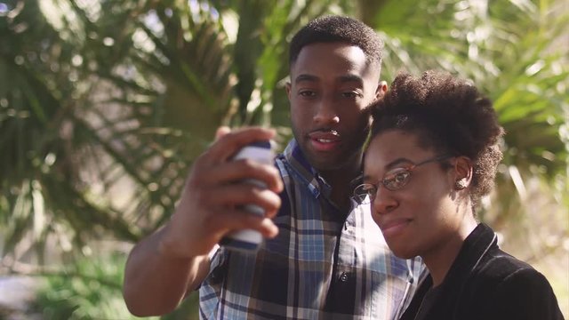 African American couple taking a cell phone picture together in front of a palm tree