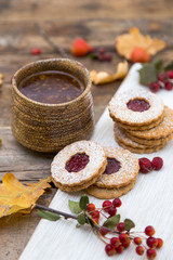 Autumn tea time. Clay mug of tea with cookies on a wooden background decorated with autumn berries and oak leaves. 