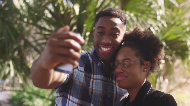 African American couple taking a cell phone picture together in front of a palm tree
