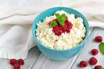 Cottage cheese in blue bowl with raspberries jam and mint on wooden background