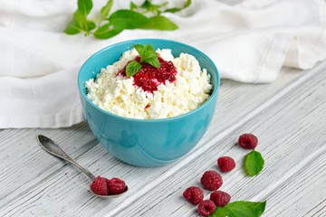 Cottage cheese in blue bowl with raspberries jam and mint on wooden background