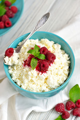 Cottage cheese in blue bowl with raspberries jam and mint on wooden background