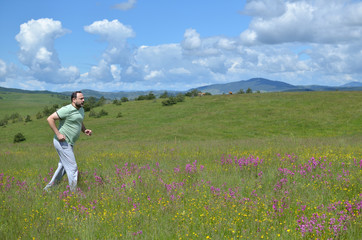 Fototapeta premium Man jogging over a meadow on Zlatibor Mountain, while clouds forming shape of heart on sky above his head