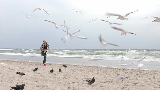 Woman feeding birds at the beach on a cloudy day, slow motion, wide shot